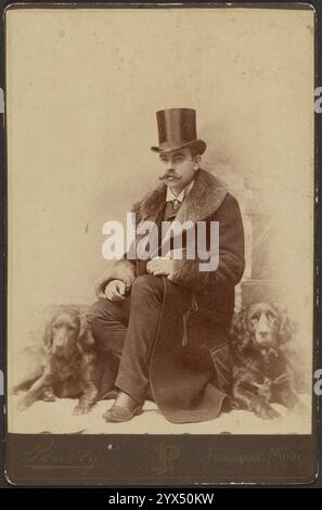 Portrait d'un homme moustachié assis en chapeau haut et hiver, manteau à col de fourrure avec un Cocker Spaniel Dog reposant des deux côtés, vers 1890. Banque D'Images