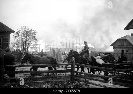 Russie 1943 soldats allemands en retraite sur des véhicules tirés par des chevaux devant des maisons en feu dans un village de la région des marais de Pripjet entre Mogilev, Bobruiks et Rogachev. En raison de l'ordre de la terre brûlée, les colonies et les approvisionnements ont été détruits pendant la retraite. Centre du groupe d'armées, dans la zone de la 110e division d'infanterie. [traduction automatique] Banque D'Images