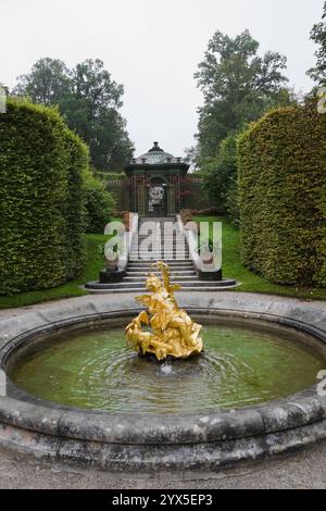 Fontaine d'eau avec sculpture dorée dans le parterre bordé par des haies d'arbres feuillus et des escaliers dans le jardin formel du palais Linderhof à la fin de l'été. Banque D'Images