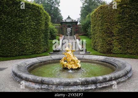 Fontaine d'eau avec sculpture dorée dans le parterre bordé par des haies d'arbres feuillus et des escaliers dans le jardin formel du palais Linderhof à la fin de l'été. Banque D'Images