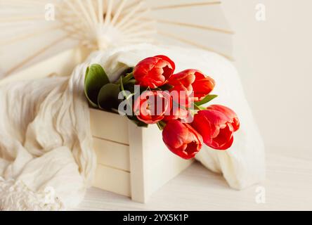 Tulipes dans une boîte en bois avec écharpe blanche et parasol Banque D'Images