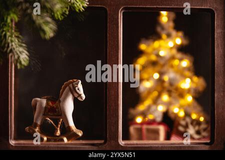 Composition de Noël avec un jouet cheval à bascule vintage au premier plan, avec un sapin de noël flou et illuminé et des cadeaux visibles à travers Banque D'Images