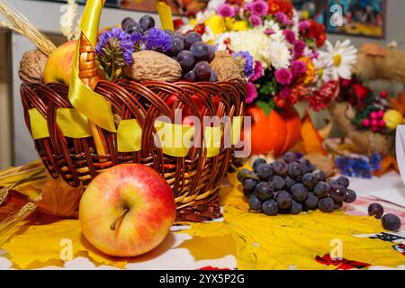 Un panier magnifiquement agencé contient des pommes, des raisins et des noix vibrantes, accompagnés de fleurs colorées. Cet affichage festif reflète la joie du ha Banque D'Images