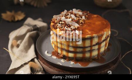 Gâteau en couches arrosé de sauce caramel, garni de pacanes et de flocons de noix de coco. Banque D'Images