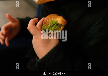 La main de Сhild tient un croissant avec une feuille de laitue. Une bonne nutrition pour les enfants d'âge préscolaire. Restauration rapide et collations saines pour les enfants. Livraison de nourriture prête à l'emploi Banque D'Images