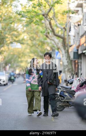 Un jeune couple chinois dans la vingtaine marche sur le trottoir dans le district de Hongkou, Shanghai, République populaire de Chine, dans la soirée, décembre 2024, du Banque D'Images