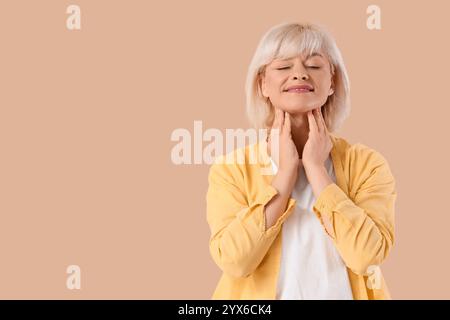 Femme mature auto-examinant la glande thyroïde sur fond beige Banque D'Images