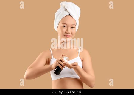 Jeune femme asiatique en serviette appliquant de la mousse nettoyante sur fond beige Banque D'Images