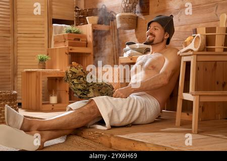 Bel homme avec fouet relaxant dans le sauna Banque D'Images