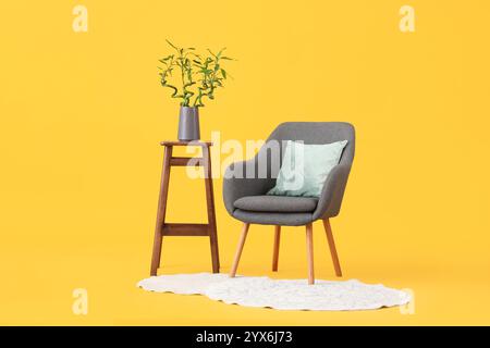 Table avec tiges de bambou dans vase, fauteuil et tapis sur fond jaune Banque D'Images