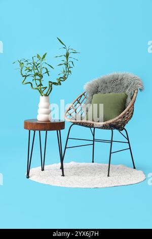 Table avec tiges de bambou dans vase, fauteuil et tapis sur fond bleu Banque D'Images