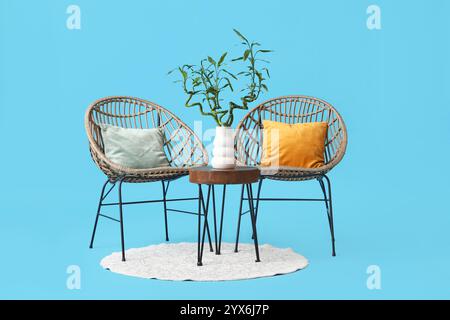 Table avec tiges de bambou dans vase, fauteuils et tapis sur fond bleu Banque D'Images