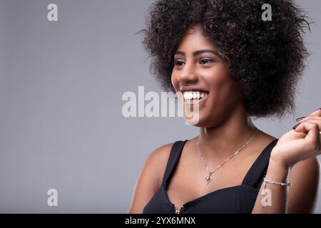Portrait de studio mettant en scène une jeune femme joyeuse avec de beaux cheveux afro, souriant brillamment tout en regardant loin, rayonnant de bonheur et émoti positif Banque D'Images
