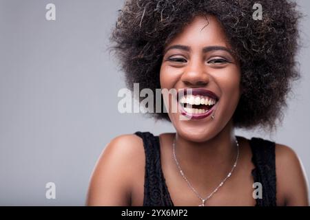 Portrait studio mettant en scène une jeune femme joyeuse aux cheveux afro, souriant largement et révélant ses dents, rayonnant de bonheur et de joie dans une exp vibrante Banque D'Images