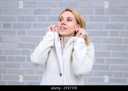 Une femme blonde vêtue d'un manteau blanc regarde vers le haut avec un sourire éclatant et joyeux. Banque D'Images