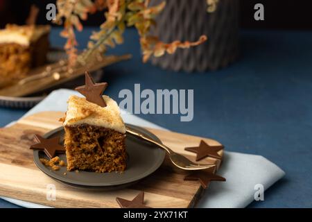 Une tranche de gâteau aux carottes avec un glaçage crémeux et un topper chocolat en forme d'étoile, servi sur une petite assiette avec une cuillère. Banque D'Images