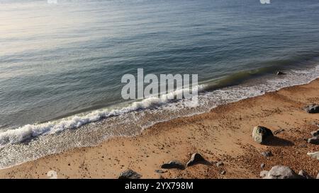 Vagues légères débarquant sur une plage de sable et rocheuse. Grand angle. Banque D'Images