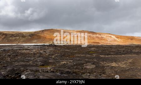Paysage volcanique de Leirhnjukur, zone géothermique de Myvatn en Islande, avec des champs de lave noire et des collines orangées de sol minéral. Banque D'Images