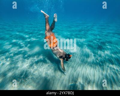 Un homme libre plonge dans une eau turquoise cristalline, maillots de bain orange visibles. Banque D'Images
