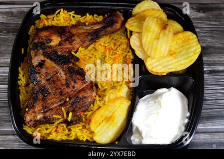 Cuisine arabe syrienne de poulet grillé au charbon de bois grillé au barbecue avec riz basmati coloré et frites de pommes de terre frites, servi dans une assiette noire jetable, s. Banque D'Images