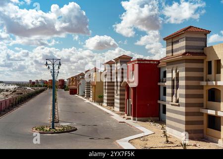 Villas colorées avec des façades rayées et des toits de tuiles bordent une rue calme du Blue Porto Matruh Resort à Mersa Matruh, en Égypte, sous un ciel bleu vif. Banque D'Images