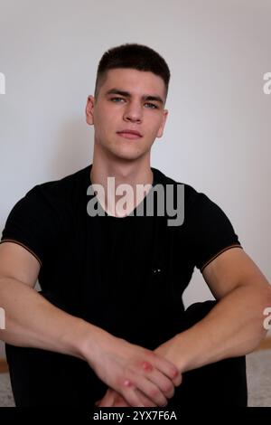 jeune homme occasionnel assis avec les jambes croisées et tenant la tête tout en souriant à la caméra. isolé sur blanc Banque D'Images