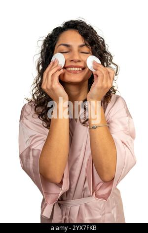 Femme heureuse portant un peignoir en utilisant des tampons de coton pour enlever le maquillage, profitant de sa routine de soins de la peau Banque D'Images