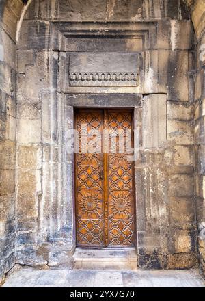 Une porte en bois magnifiquement conçue présente des motifs géométriques détaillés, nichée dans un mur de pierre altérée, mettant en valeur l'architecture historique et l'artisanat Banque D'Images