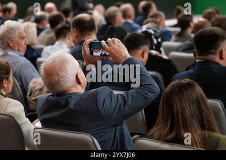 Public participant à un séminaire pendant qu'un individu mature capture des moments à l'aide d'un smartphone. Affaires, partage professionnel et apprentissage dans un cadre formel. Banque D'Images