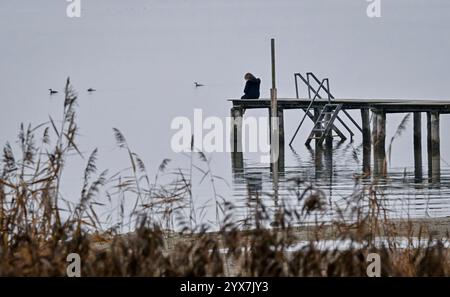 Seebruck, Allemagne. 14 décembre 2024. Une femme est assise sur une jetée près de Seebruck sur le lac Chiemsee par temps brumeux. Crédit : Uwe Lein/dpa/Alamy Live News Banque D'Images