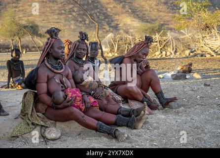 Femme Himba mariée avec leurs bébés dans leurs bras assis devant la cabane de la première femme, le matin, village traditionnel Himba, Kaokove Banque D'Images