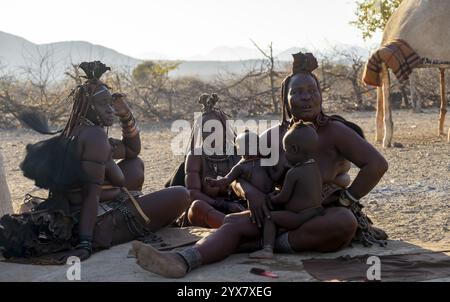 Femme Himba mariée avec leurs bébés dans leurs bras assis devant la cabane de la première femme, le matin, village traditionnel Himba, Kaokove Banque D'Images