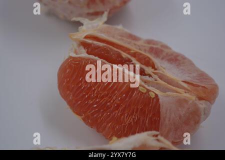 Nourriture saine et saine, beaux fruits frais. La chair rouge du pamplemousse avec de grandes tranches blanches est située sur un fond plastique blanc. Banque D'Images