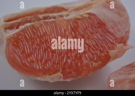 Nourriture saine et saine, beaux fruits frais. La chair rouge du pamplemousse avec de grandes tranches blanches est située sur un fond plastique blanc. Banque D'Images