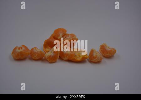 Nourriture saine, saine, épicerie, fruits frais. De nombreuses tranches de mandarine orange avec de la peau de mandarine orange pelée sont sur un fond en plastique blanc. Banque D'Images