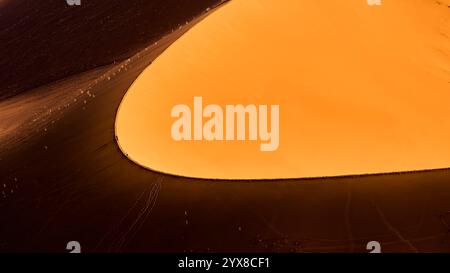 Au loin, les gens marchent sur la crête d’une dune, de fortes ombres comme on le voit depuis Big Daddy Dune, Sossusvlei, Sesriem National, Namibie, Afrique. Banque D'Images