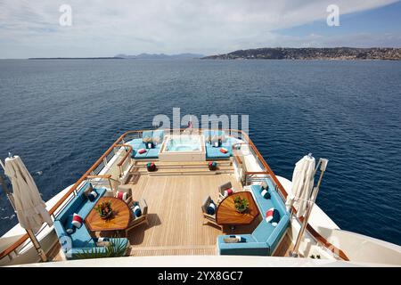 Spacieux pont de yacht avec un jacuzzi luxueux entouré de sièges, avec une vue imprenable sur l'océan et le paysage côtier lointain. Banque D'Images