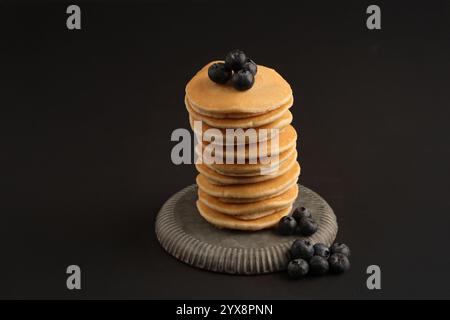 Studio image sur fond noir d'une pile de crêpes sur une plaque de style étain surmontée de bleuets mûrs. Banque D'Images