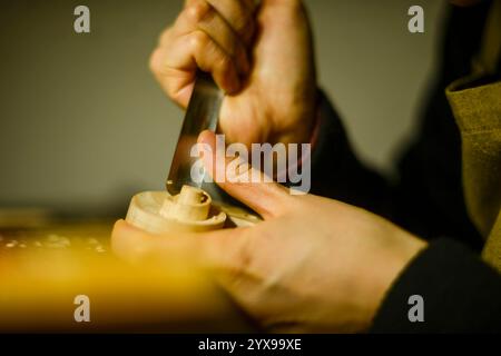 Luthier sculpte méticuleusement un morceau de bois, à l'aide d'un ciseau pointu, démontrant la précision et le savoir-faire impliqués dans la création d'instrume musical Banque D'Images