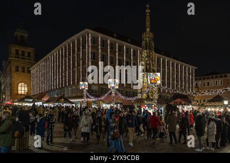 Nürnberger Christkindlesmarkt, 14.12.2024 Abendaufnahme des Christkindlesmarktes auf dem Hauptmarkt. IM Zentrum des Bildes steht der beleuchtete Schöne Brunnen, umgeben von Marktständen mit weihnachtlicher Dekoration. Menschen spazieren und verweilen vor den festlich geschmückten Marktständen. IM Hintergrund ist das Rathaus mit seinen Lichterketten Nürnberg Bayern Deutschland *** Nuremberg Christkindlesmarkt, 14 12 2024 cliché du soir du Christkindlesmarkt sur le marché principal au centre de l'image se trouve le Schöne Brunnen illuminé, entouré d'étals de marché avec des décorations de Noël Banque D'Images