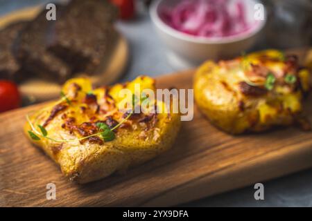 Pommes de terre cuites au four avec fromage et bacon écrasées sur une planche de bois sur une table grise avec une boîte de hareng, des oignons rouges marinés et du pain de seigle. Haute qualité p Banque D'Images