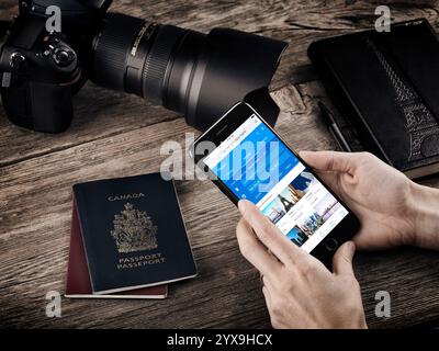 Femme la main avec Apple iPhone 7 Afficher l'information de vol sur une table avec les passeports, un appareil photo et un ordinateur portable, les voyages la vie encore conceptuel Banque D'Images