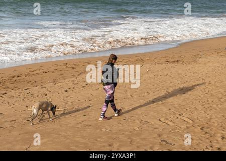 Une femme promène un chien tout en envoyant des SMS sur son téléphone portable sur la Playa de Zarautz à Zarautz, pays Basque, Espagne. Le village de villégiature populaire se trouve le long de t Banque D'Images