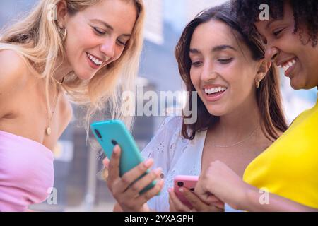Trois amis enthousiastes regardant un smartphone à l'extérieur. Banque D'Images