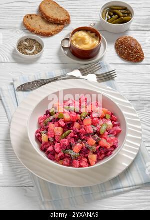 Rosolli, salade traditionnelle finlandaise de Noël festive dans un bol blanc sur une table en bois blanc avec fourchettes, pain de seigle et vinaigrette végétalienne maison, v Banque D'Images