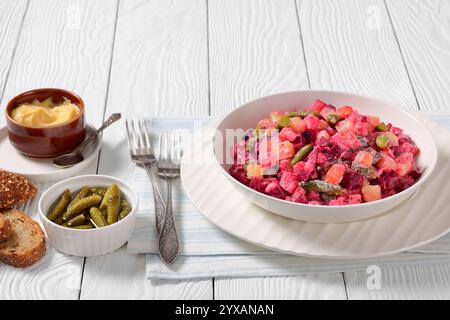 Rosolli, salade traditionnelle finlandaise de Noël festive dans un bol blanc sur une table en bois blanc avec fourchettes, pain de seigle et vinaigrette maison, vue paysage f Banque D'Images