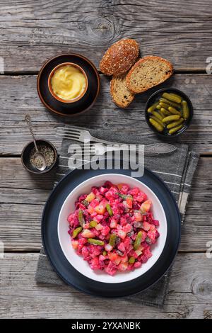 Rosolli, salade de Noël traditionnelle finlandaise dans un bol blanc sur une table en bois rustique avec fourchettes, pain de seigle et vinaigrette végétalienne maison, verticale Banque D'Images