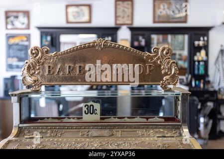 Gros plan d'une caisse enregistreuse vintage avec un signe décoratif « Barber Shop » et des gravures complexes, dans un salon de coiffure classique. Banque D'Images