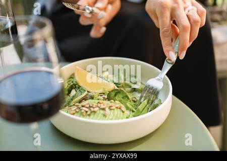 Gros plan d'une femme mangeant de la salade verte avec de l'avocat et un verre de vin rouge sur une terrasse d'été Banque D'Images