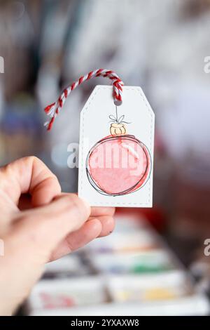Gros plan d'une personne tenant une étiquette cadeau de Noël avec des boules de Noël peintes à l'aquarelle Banque D'Images